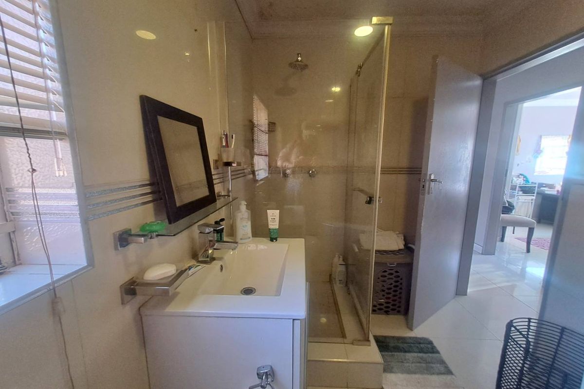 A functional bathroom featuring a vanity with basin, a glass-enclosed shower, and neutral wall and floor tiling.