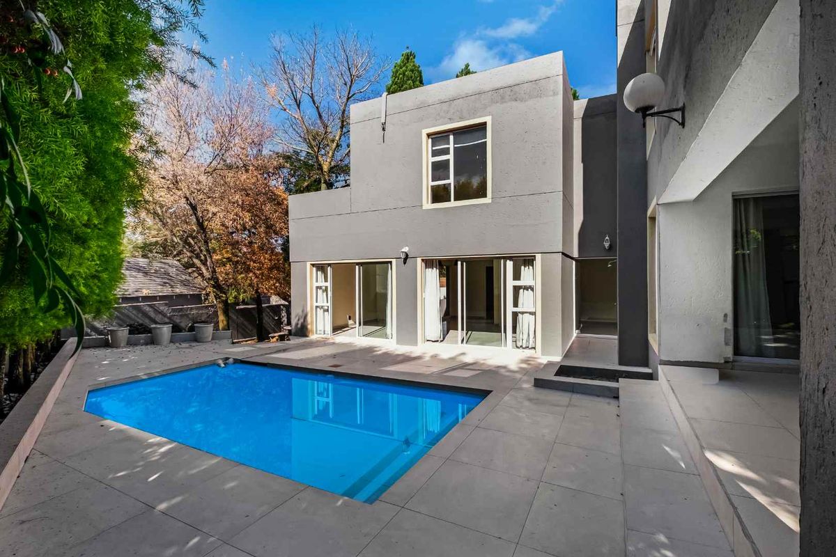 Rear view of a modern two-story house featuring a swimming pool, paved patio area, and large sliding glass doors leading to the interior.