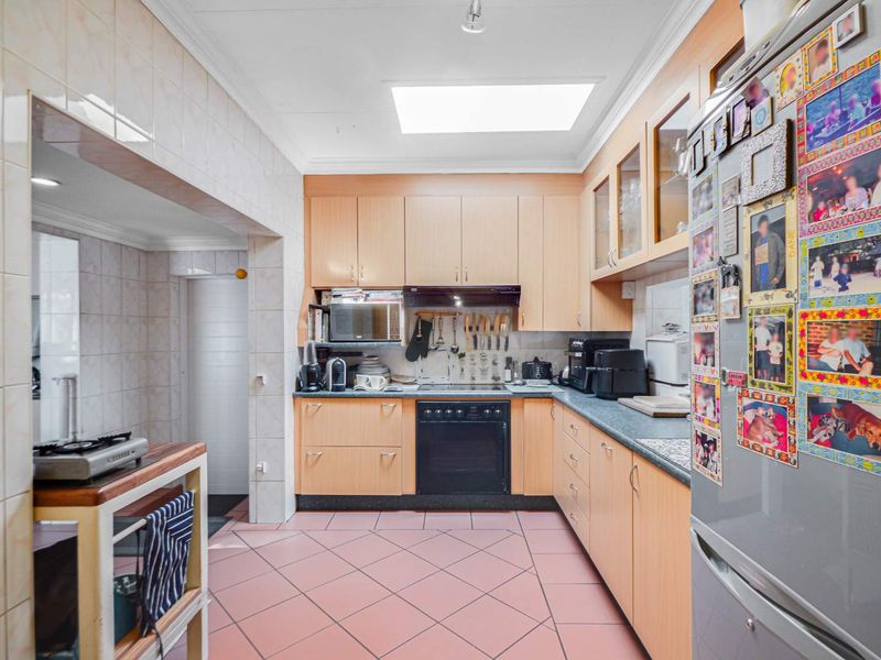 A functional kitchen featuring light wood cabinetry, laminate countertops, tiled flooring, and a skylight, providing a practical workspace with integrated cooking appliances.