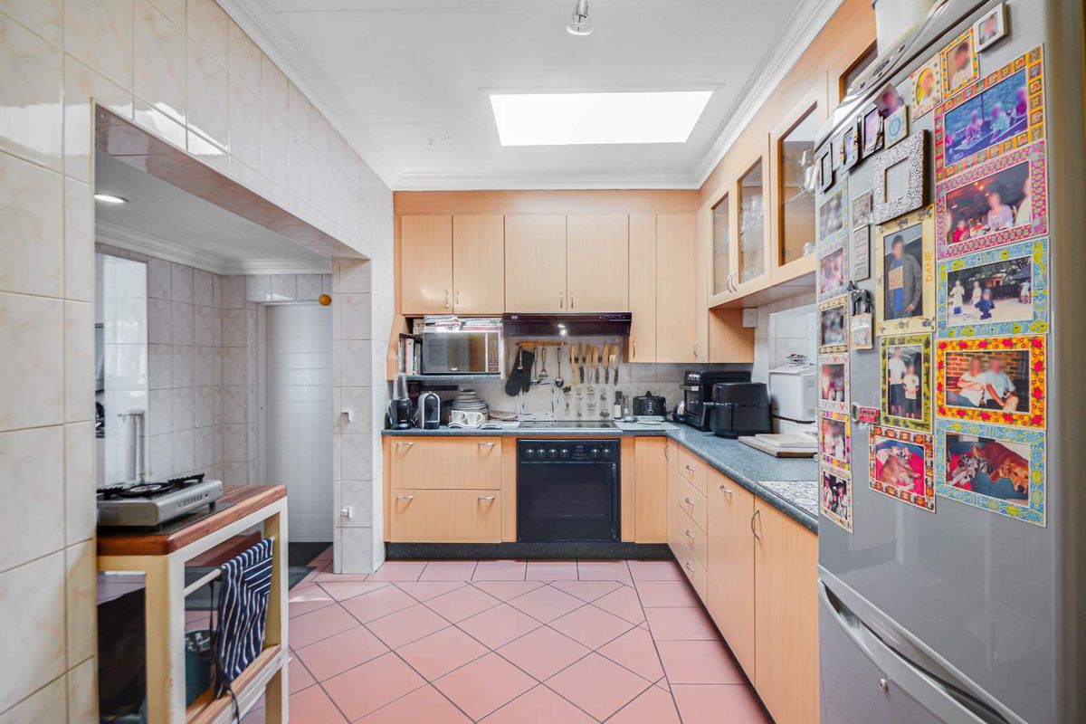 A functional kitchen featuring light wood cabinetry, laminate countertops, tiled flooring, and a skylight, providing a practical workspace with integrated cooking appliances.