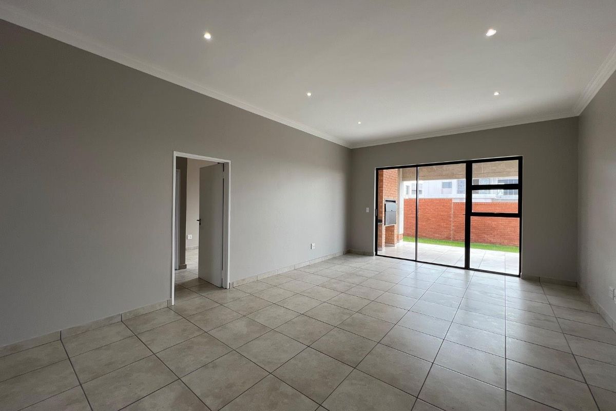 Spacious, neutral-toned living area featuring large sliding glass doors that open onto a covered patio and garden.