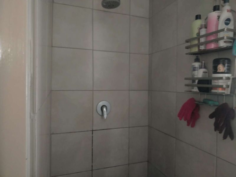 A shower enclosure featuring neutral ceramic wall tiles, a standard shower mixer, and a fixed shower head.