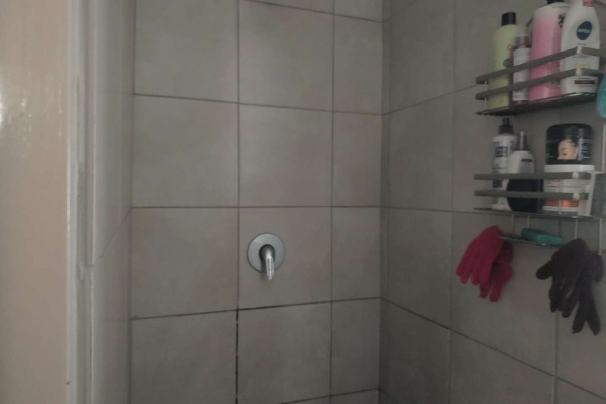 A shower enclosure featuring neutral ceramic wall tiles, a standard shower mixer, and a fixed shower head.
