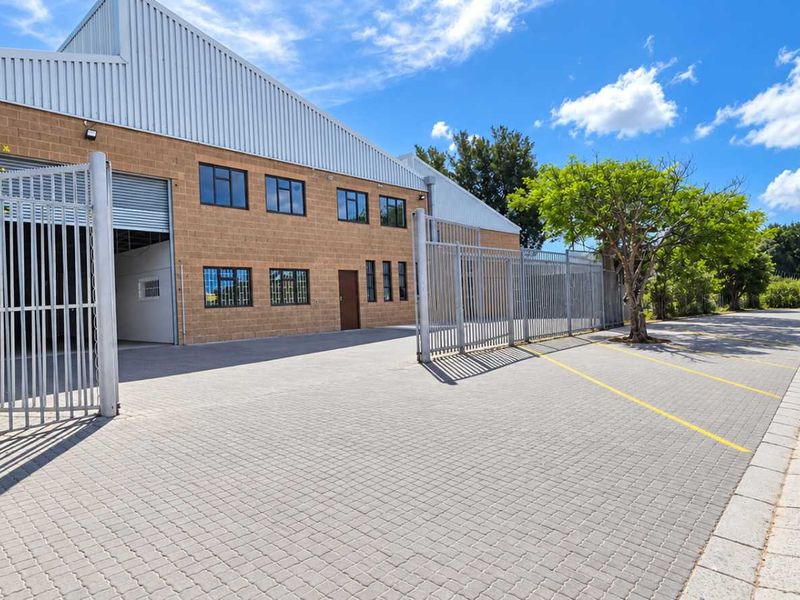Industrial property exterior featuring a paved driveway, secure perimeter fencing, and a large metal roller shutter door for easy access.