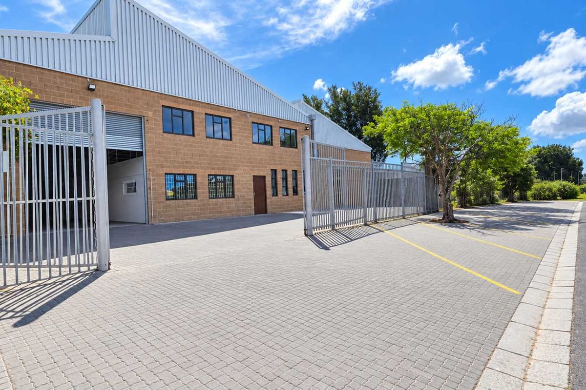 Industrial property exterior featuring a paved driveway, secure perimeter fencing, and a large metal roller shutter door for easy access.