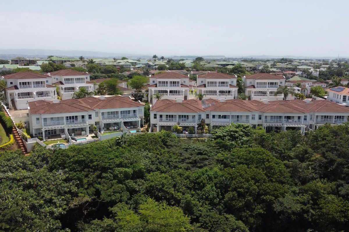 Aerial view of a residential apartment complex featuring multiple buildings with tiled roofs, balconies, and private garden spaces.