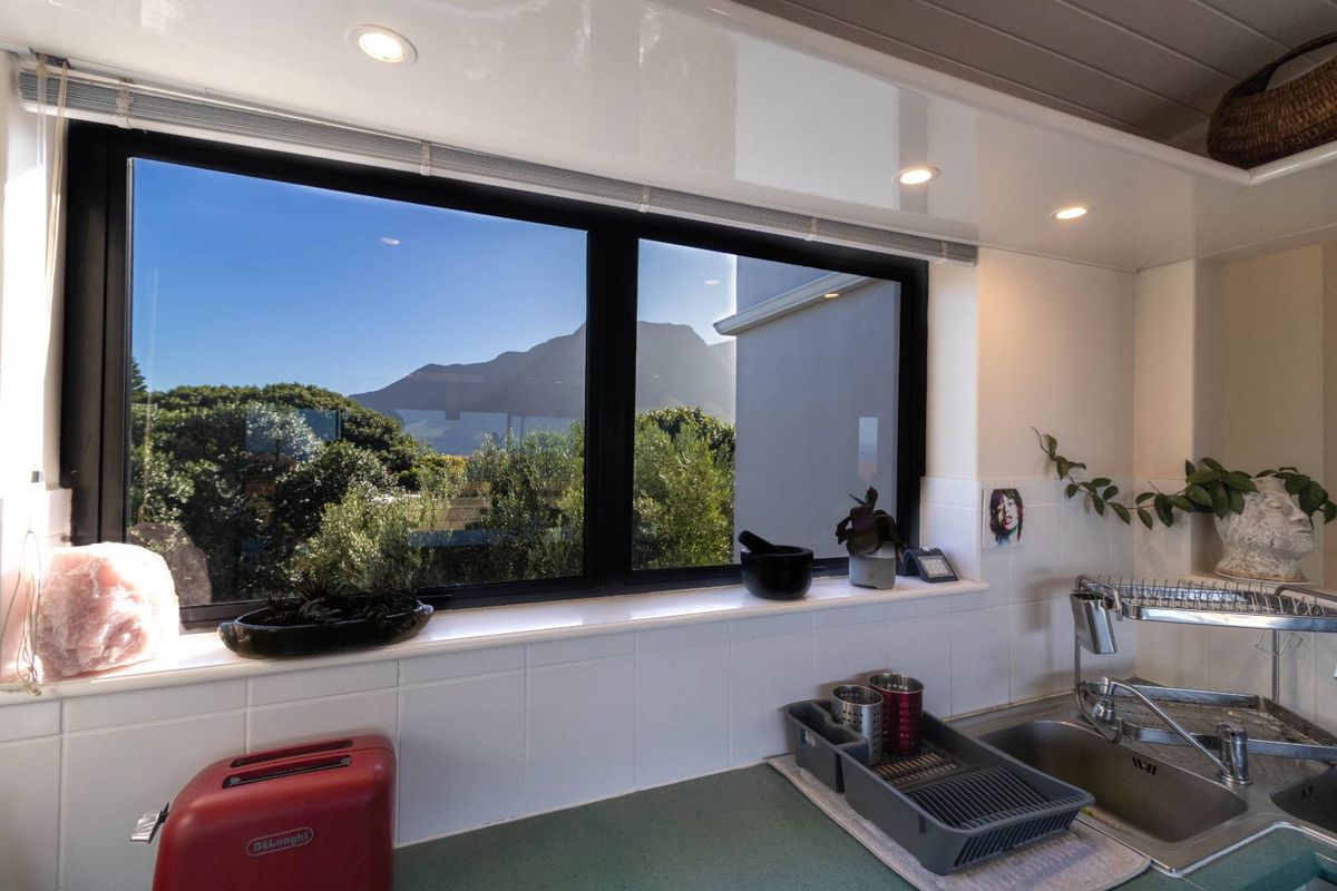A bright kitchen area featuring a large window with scenic mountain views, a stainless steel sink, and tiled splashbacks.