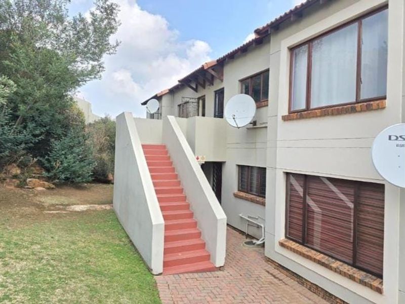 Rear exterior view of a townhouse featuring an external staircase, brick paved walkway, and established garden area.