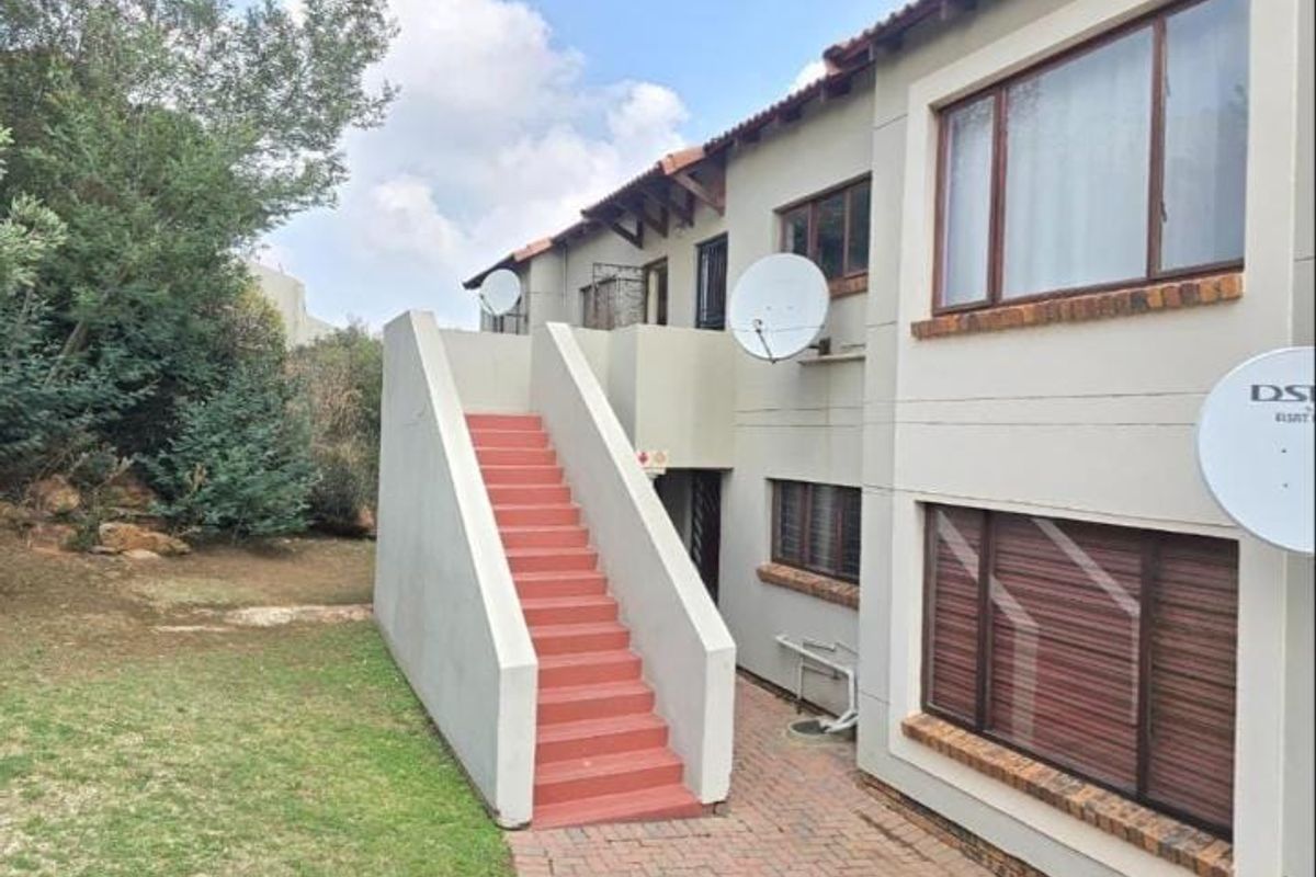Rear exterior view of a townhouse featuring an external staircase, brick paved walkway, and established garden area.