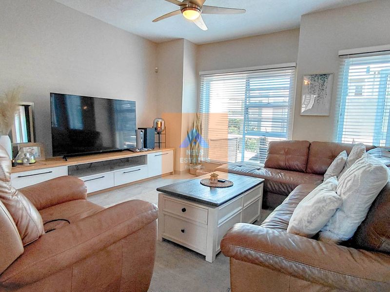 A comfortable living room featuring a ceiling fan, large windows with venetian blinds, and access to an outdoor area via a sliding glass door.