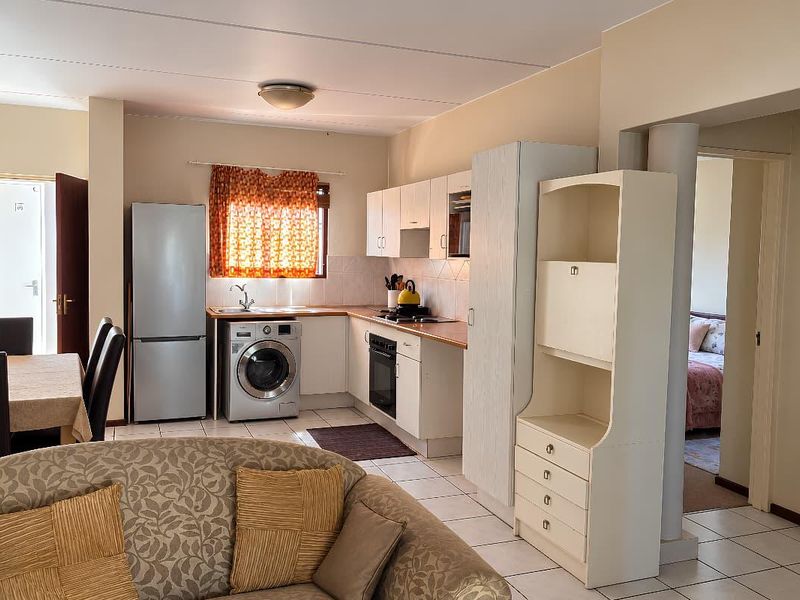 Open plan living and kitchen area featuring tiled flooring, built-in cabinetry, integrated appliances, and direct access to adjacent rooms.