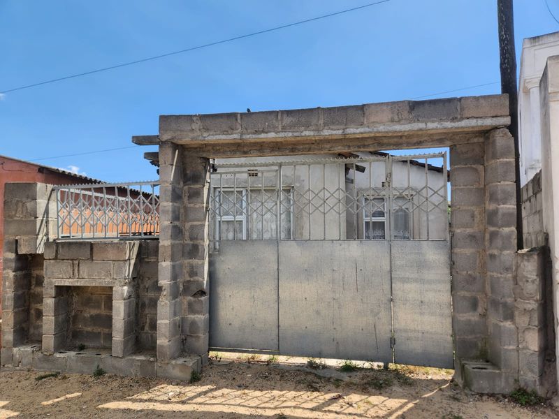 Front entrance view featuring a concrete block boundary wall and a metal security gate providing access to the property.