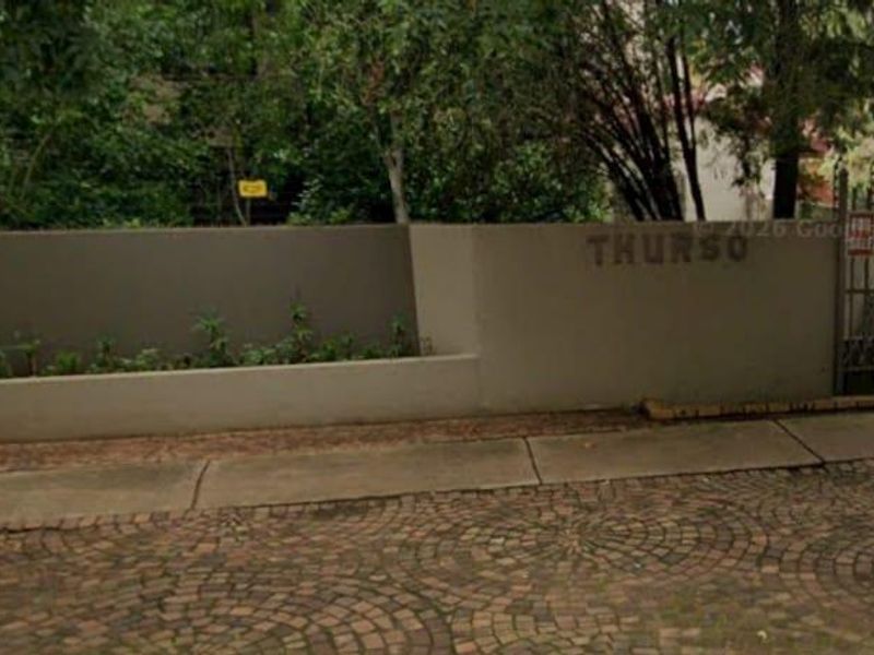 Front exterior view of the property featuring a boundary wall, metal security gate, and paved driveway access.