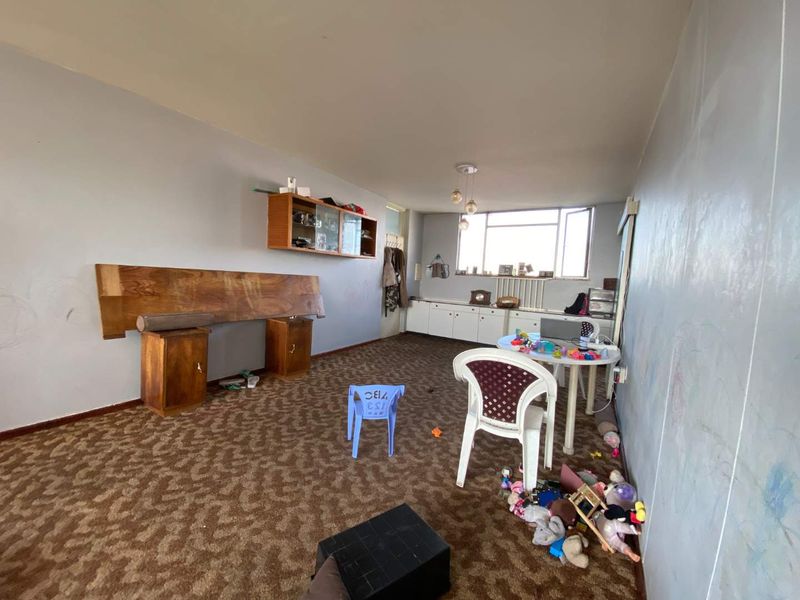 Spacious living area featuring built-in cabinetry and large windows, currently requiring cosmetic updates to the flooring and wall finishes.