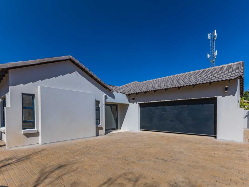 Front elevation of a modern house featuring a paved driveway, automated garage door, and clean rendered exterior walls under a tiled roof.