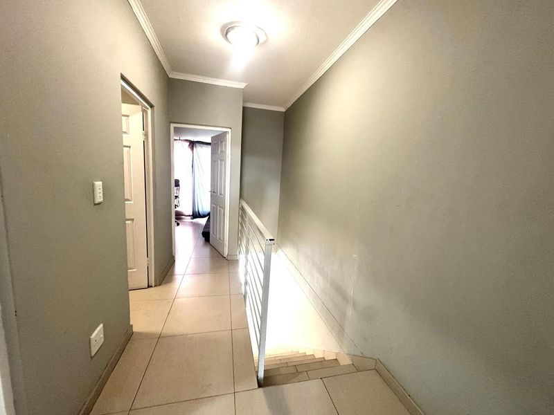 A bright, tiled hallway featuring a metal balustrade overlooking the staircase, providing access to adjacent rooms.