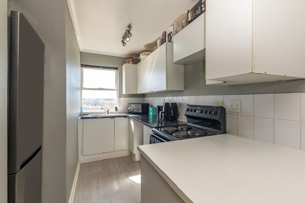 Compact kitchen featuring white cabinetry, dark countertops, a built-in stove, and a stainless steel sink with natural light.