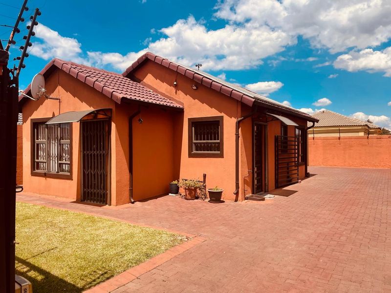 Rear view of the house featuring a paved courtyard, tiled roof, and secure perimeter with electric fencing and burglar bars.