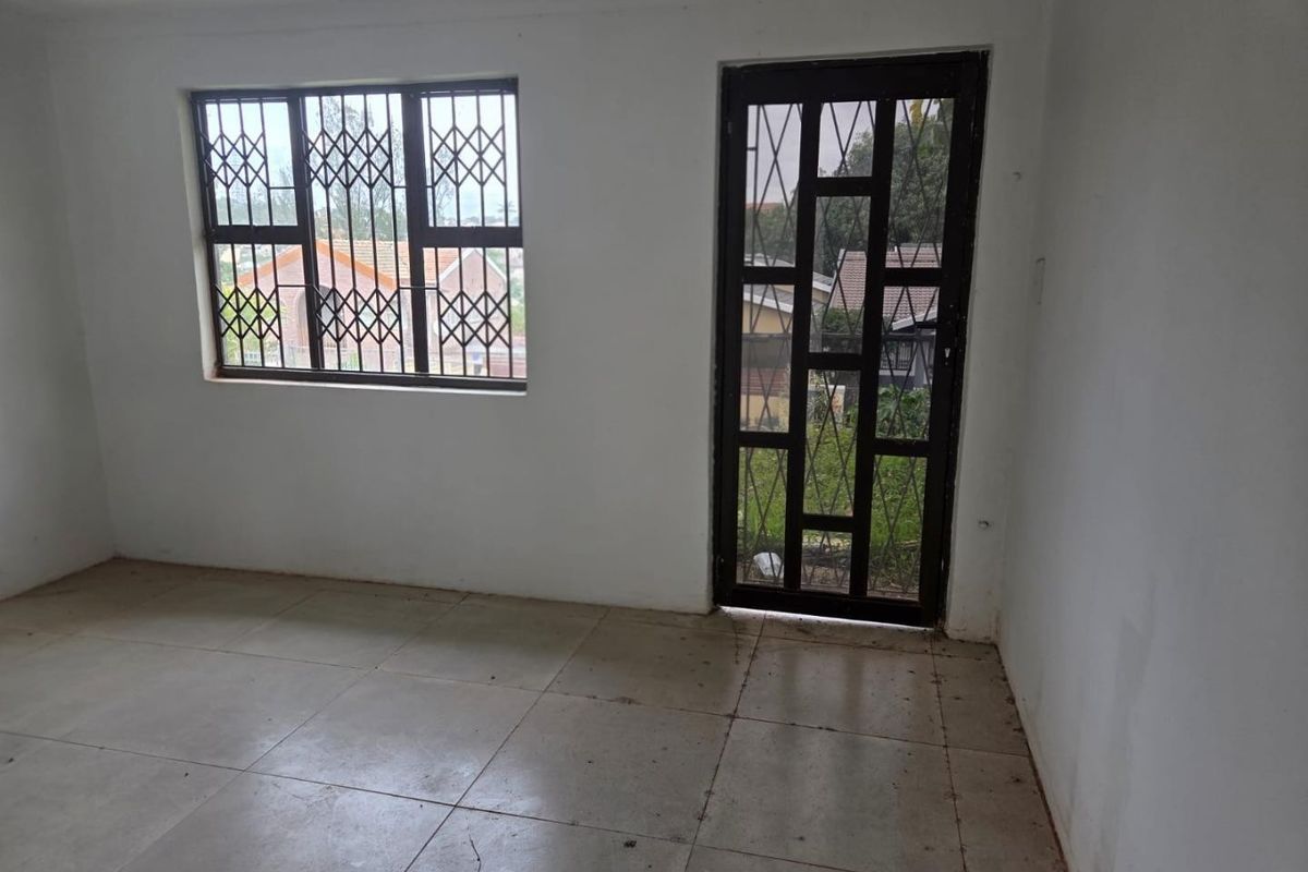 An empty living area featuring tiled flooring, a security gate, and window security bars, offering a blank canvas for potential interior design updates.