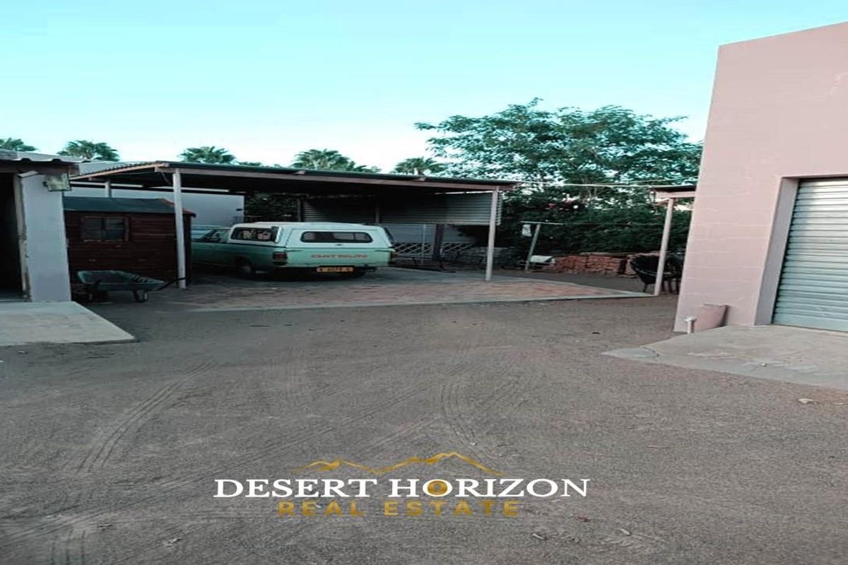 Exterior view of the property featuring a covered carport area, a roller shutter door, and an unpaved driveway space.