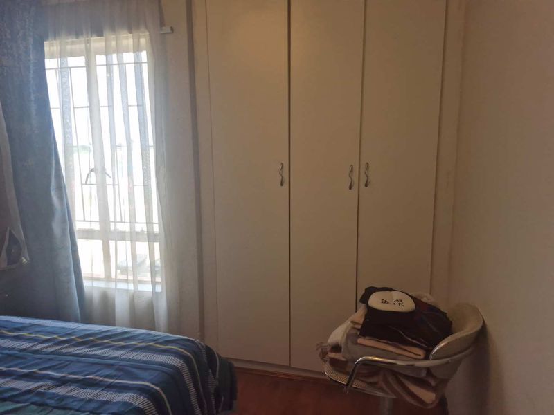 A bedroom featuring built-in cupboards and a window with security bars, providing functional storage and natural light.