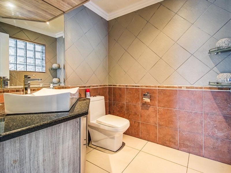 A well-maintained bathroom featuring a modern vessel sink on a granite vanity, tiled walls, and a glass block window for natural light.