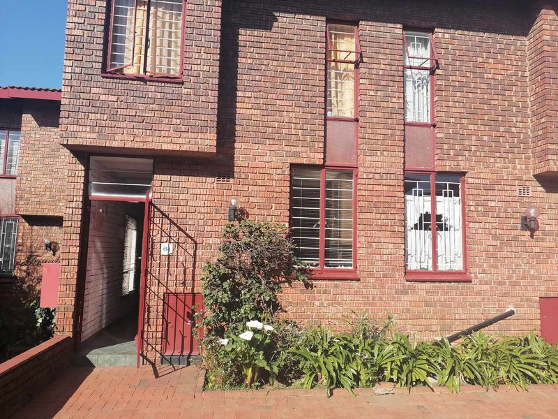 Front facade of a face brick townhouse featuring a paved entrance, security bars on windows, and external lighting.