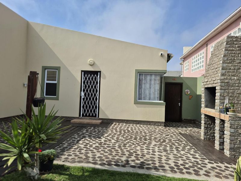 Rear exterior view featuring a paved patio area, timber decking, and a built-in brick braai, providing a functional outdoor entertainment space.