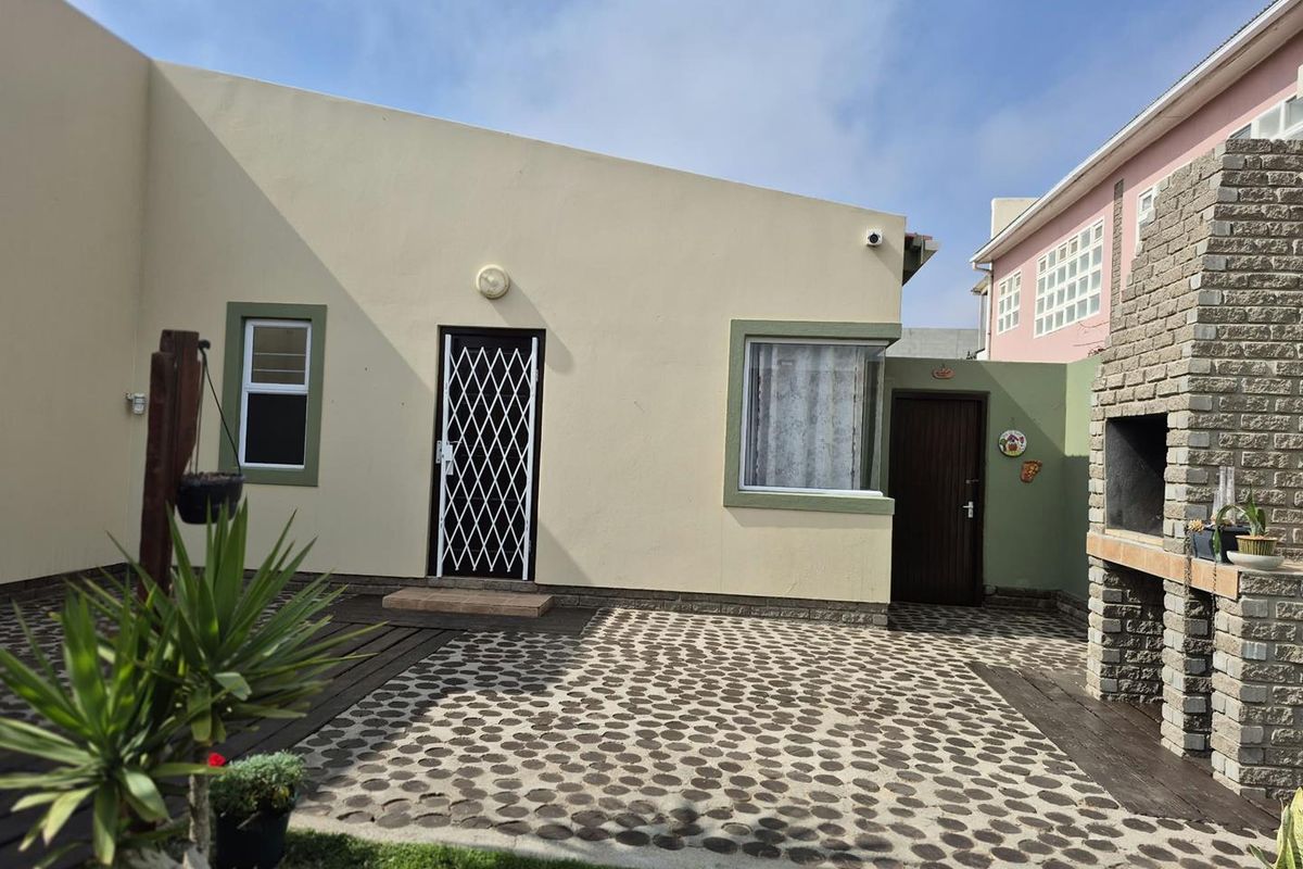 Rear exterior view featuring a paved patio area, timber decking, and a built-in brick braai, providing a functional outdoor entertainment space.