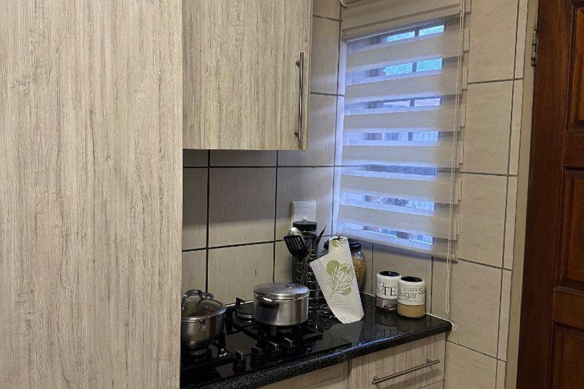 Compact kitchen area featuring light wood-grain cabinetry, granite countertops, a built-in oven, and a gas hob with tiled splashbacks.