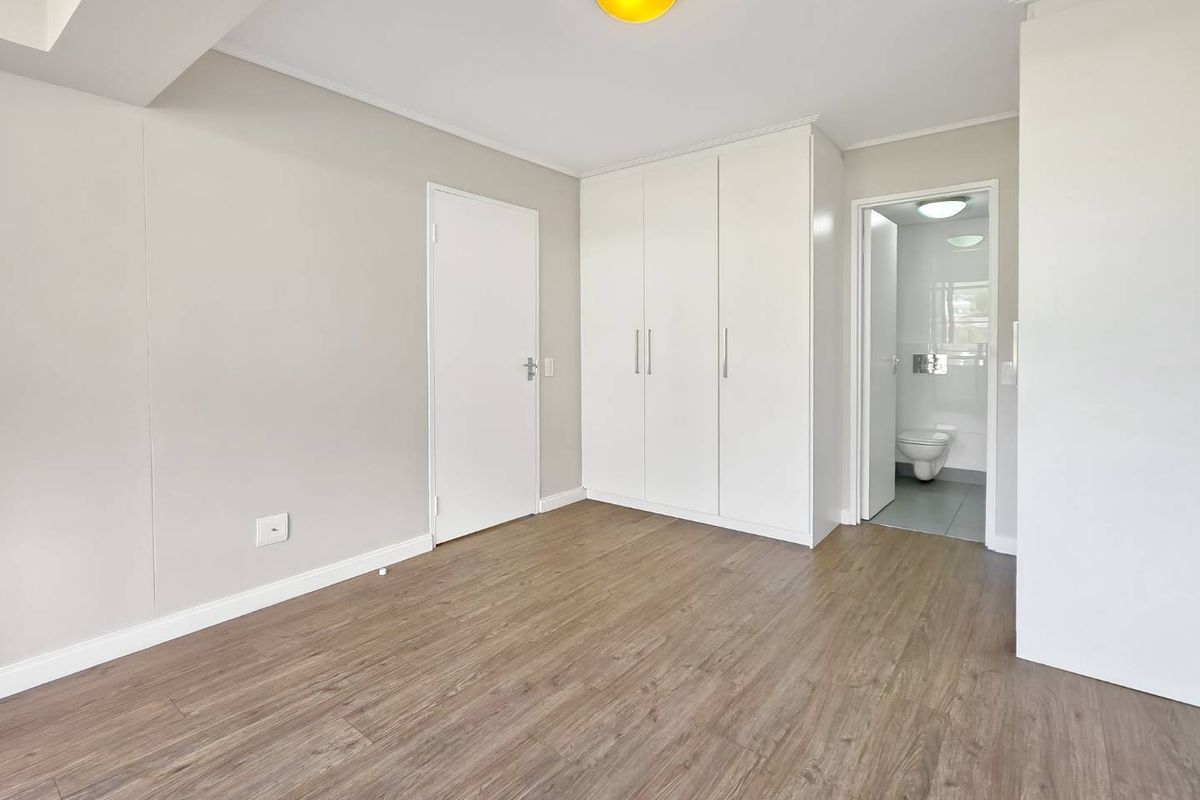 A clean, empty bedroom featuring modern laminate flooring, built-in cupboards, and direct access to an en-suite bathroom.