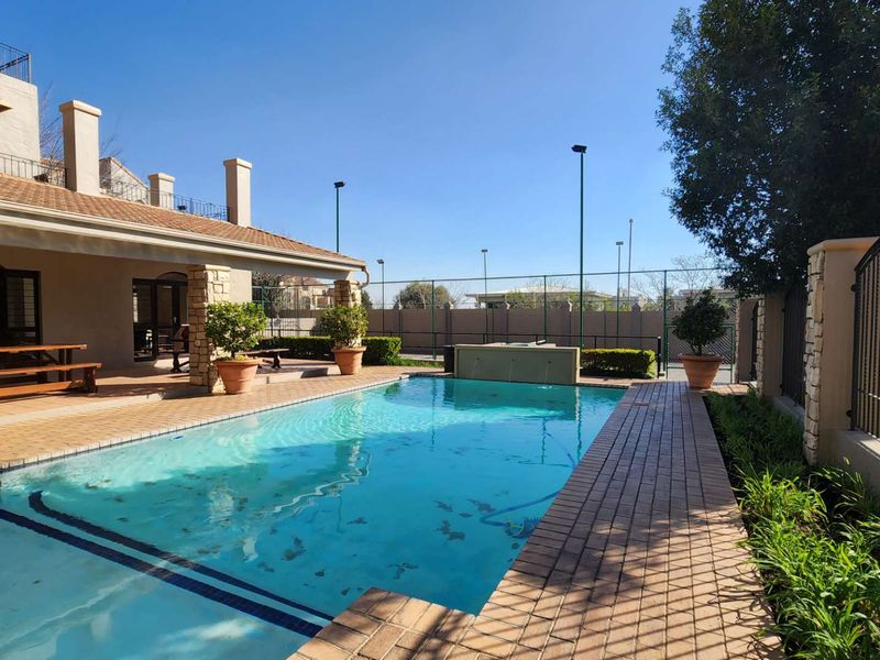 Outdoor pool area featuring a swimming pool, brick paved surround, and a covered patio with stone pillars, set within a fenced property.