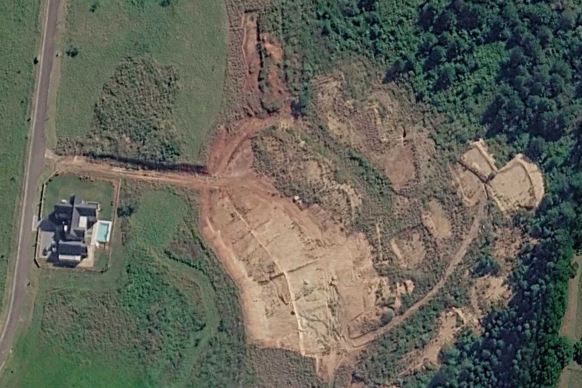 Aerial view of a large vacant commercial land plot showing cleared earth, access roads, and proximity to existing residential infrastructure.