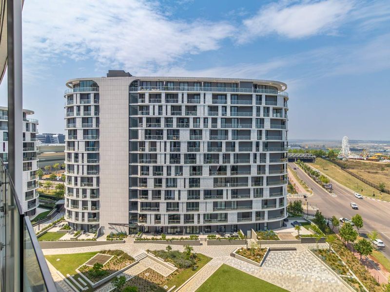 A high-angle view of a modern multi-story apartment building featuring glass balconies, a landscaped courtyard, and paved outdoor areas.
