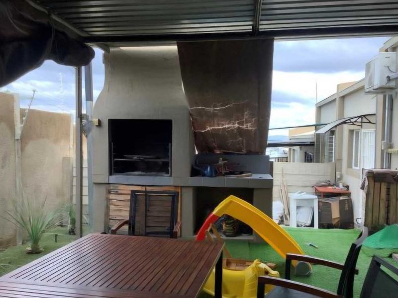 Covered outdoor patio area featuring a built-in braai and artificial grass, providing a functional space for outdoor entertaining.