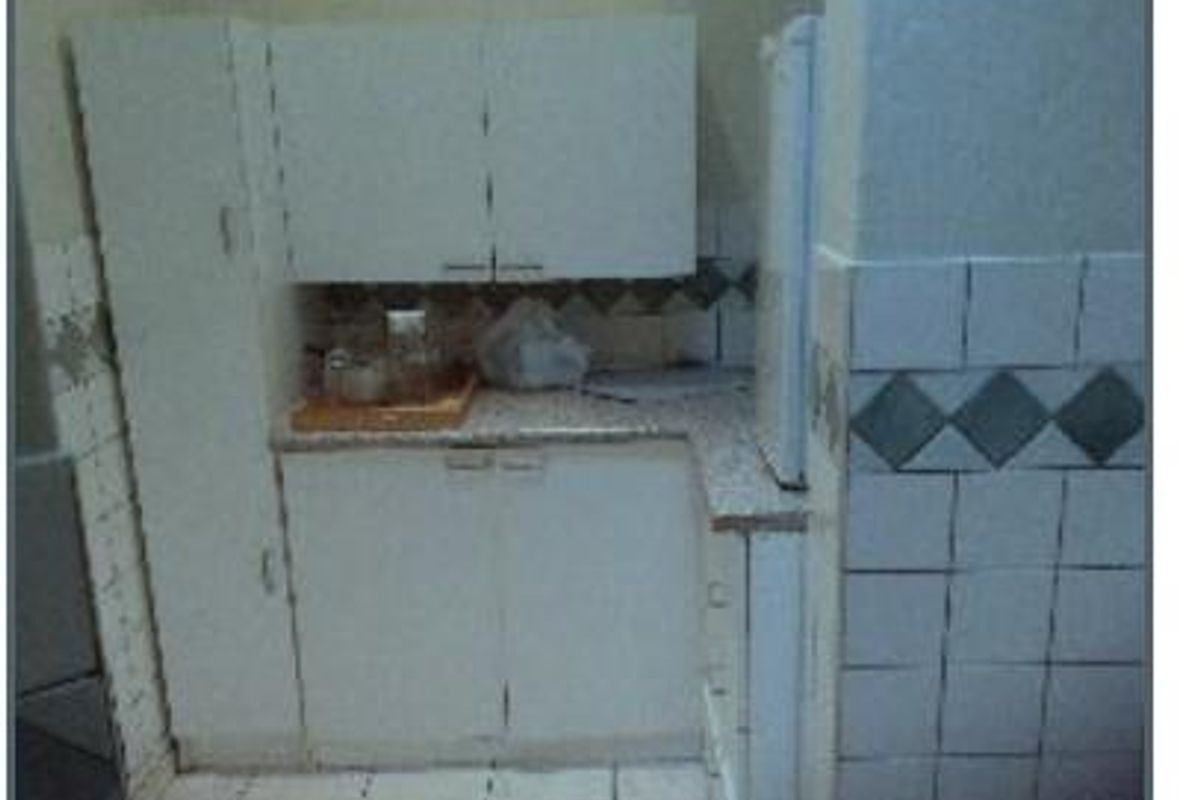 A compact office kitchenette featuring built-in white cabinetry, tiled backsplash, and tiled flooring, currently showing signs of wear and dated finishes.