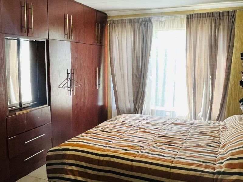 A bedroom featuring extensive dark wood built-in cupboards, tiled flooring, and natural light through a window with curtains.