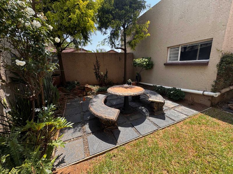A private rear garden featuring a paved patio area, established trees, and a boundary wall, offering a quiet outdoor space for relaxation.