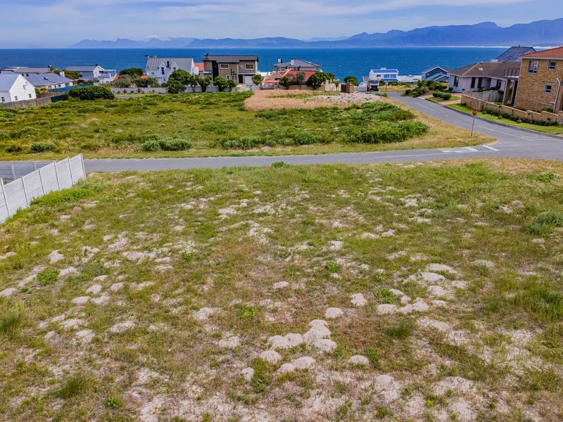 An elevated aerial view of a vacant residential plot featuring natural vegetation, a precast boundary wall, and scenic coastal and mountain views.