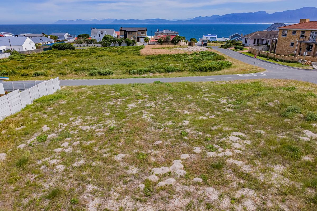 An elevated aerial view of a vacant residential plot featuring natural vegetation, a precast boundary wall, and scenic coastal and mountain views.
