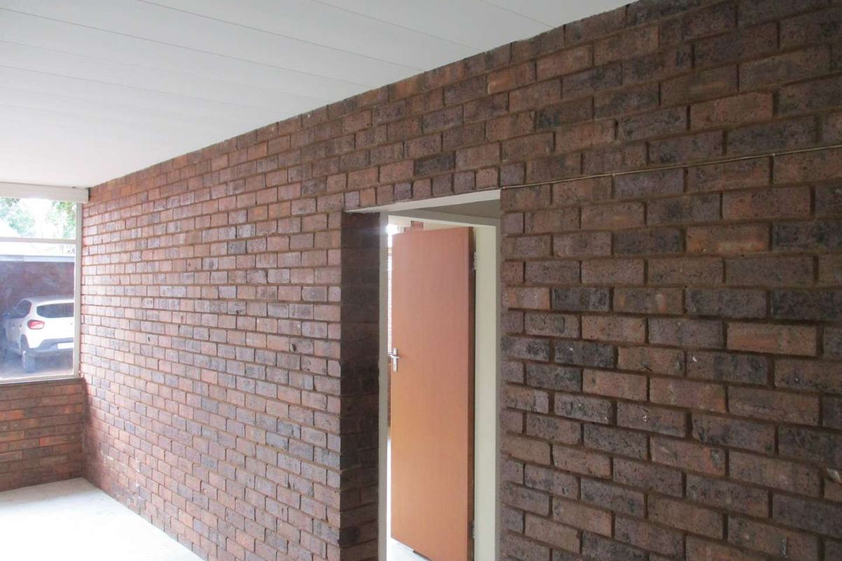 An interior view of a room featuring exposed face brick walls, a white panelled ceiling, and a doorway leading to an adjacent space.