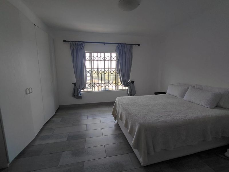 A spacious bedroom featuring neutral tiled flooring, built-in cupboards, and a window fitted with a security gate.