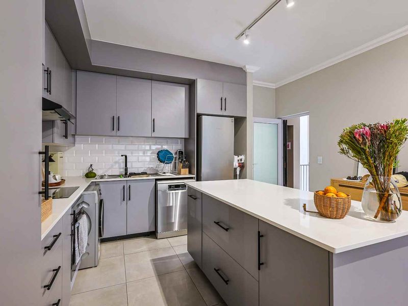 Modern kitchen featuring grey cabinetry, white subway tile backsplash, stone countertops, and a central island with integrated lighting.