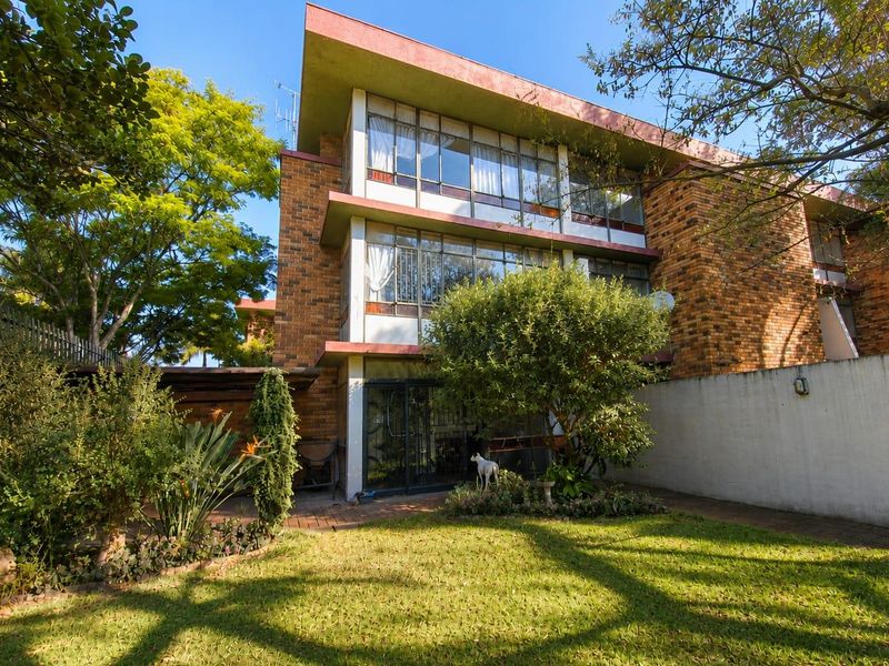 Rear view of a multi-story townhouse featuring a brick facade, large windows, a paved patio area, and a private garden space.
