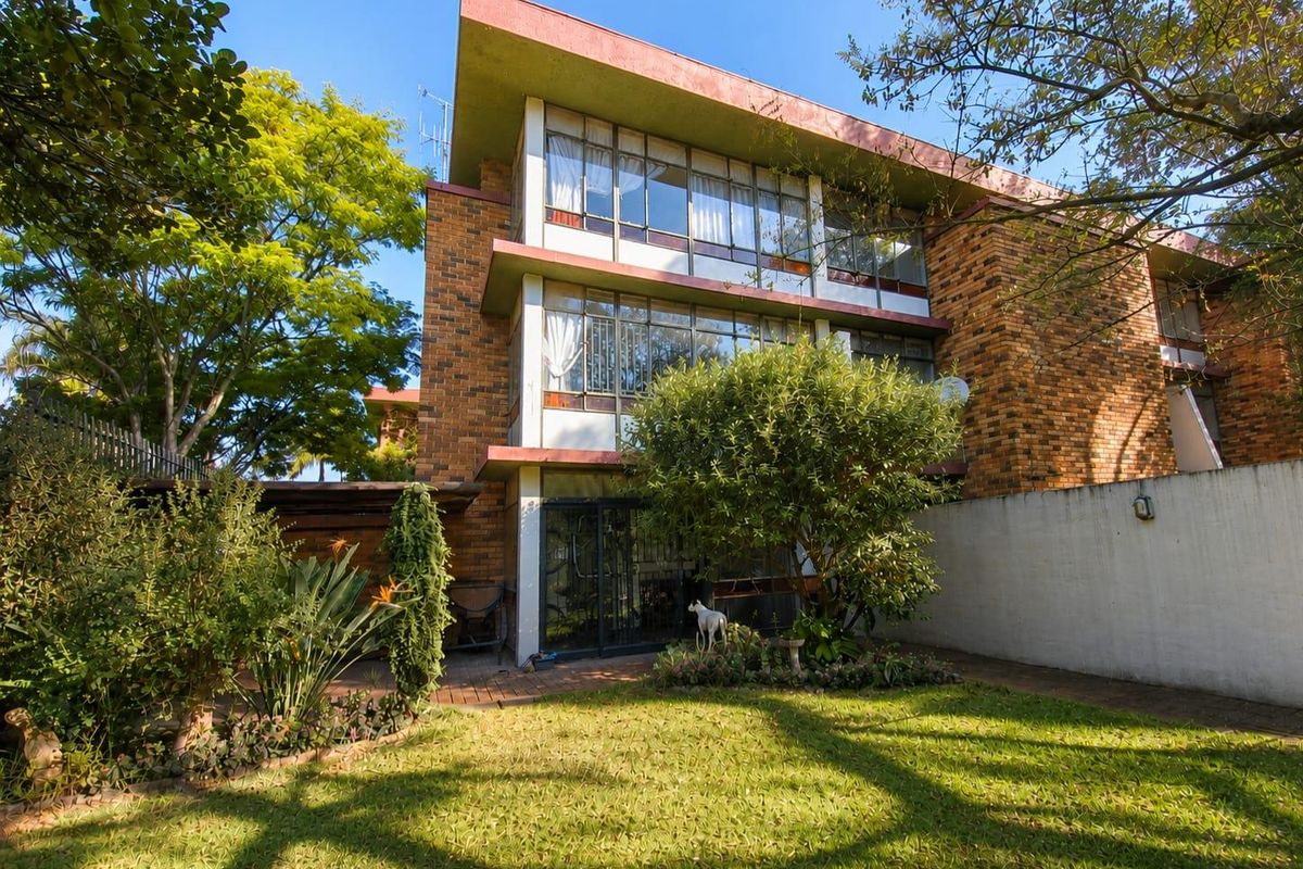 Rear view of a multi-story townhouse featuring a brick facade, large windows, a paved patio area, and a private garden space.