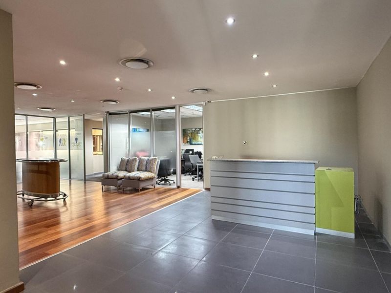 A modern office reception area featuring a built-in desk, glass partitions, and a combination of hardwood and tiled flooring with recessed lighting.