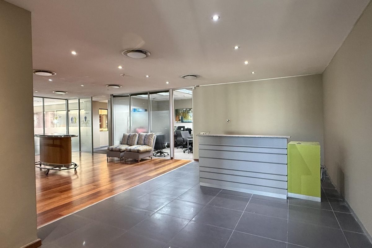 A modern office reception area featuring a built-in desk, glass partitions, and a combination of hardwood and tiled flooring with recessed lighting.
