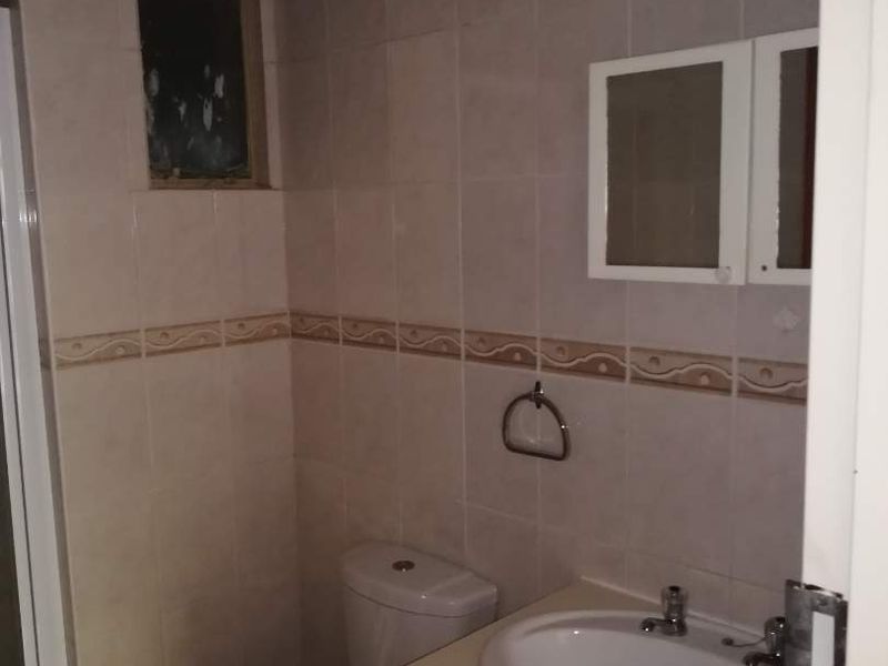 A compact bathroom featuring a vanity cabinet with integrated basin, toilet, and tiled walls, requiring cosmetic updates to modernize the space.
