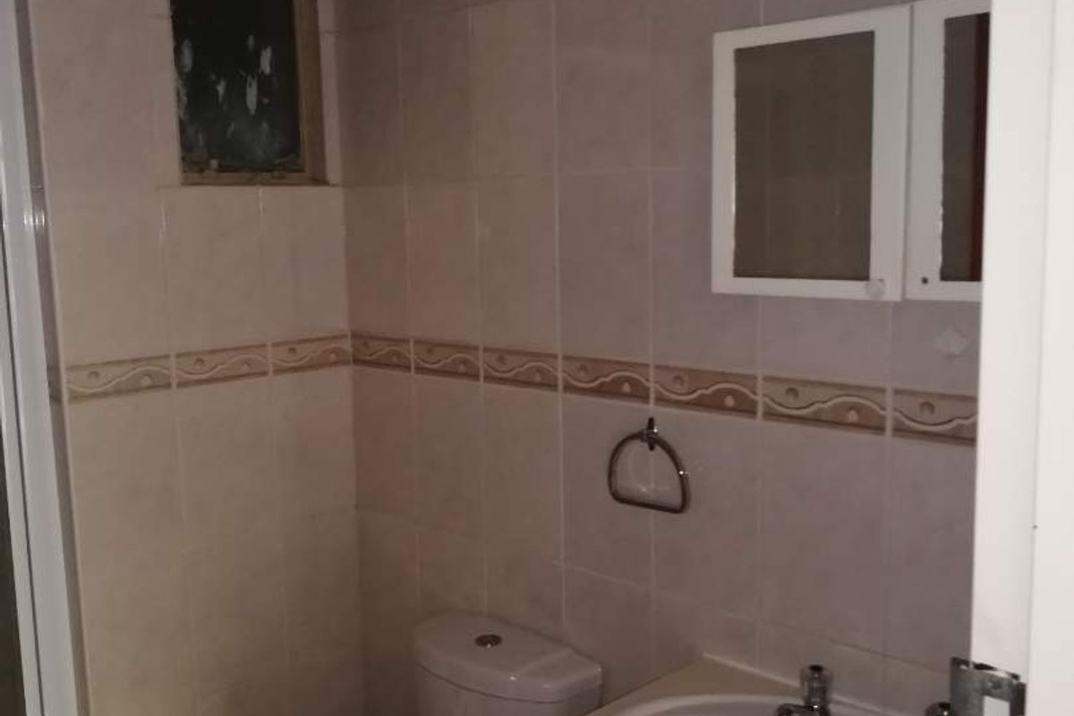 A compact bathroom featuring a vanity cabinet with integrated basin, toilet, and tiled walls, requiring cosmetic updates to modernize the space.