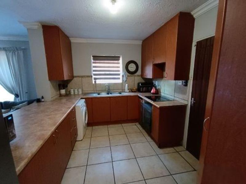 A functional kitchen featuring wooden cabinetry, laminate countertops, a double basin sink, and built-in cooking appliances with tiled flooring throughout.